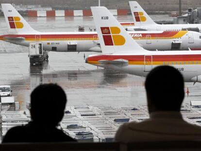 Dos pasajeros observan varios aviones de Iberia, en Barajas.