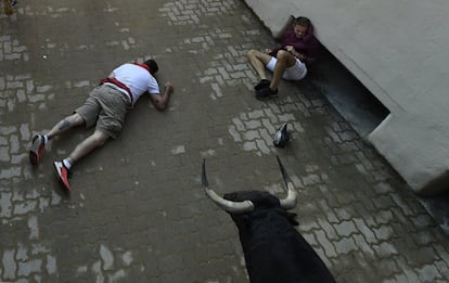 Un hombre yace inconsciente tras ser golpeado por un morlaco, mientras otro joven espera que pase el resto de la manada de toros .