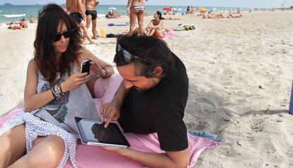 Una pareja utiliza sus dispositivos m&oacute;viles en una playa