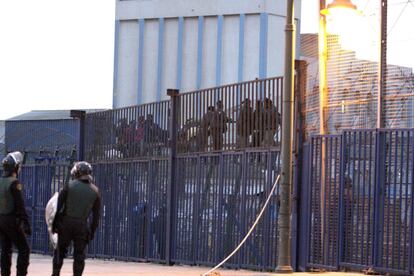 Agentes antidisturbios vigilan la valla fronteriza, donde un grupo de inmigrantes espera la posibilidad de dar el salto.