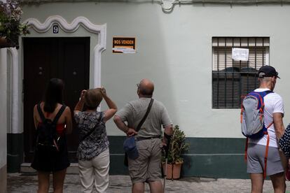 Turistas en Cádiz capital, este martes, en el barrio de El Pópulo, donde aún se conservan los carteles contra los pisos turísticos en la casa en la que hace tres meses se evitó el desahucio de una anciana.