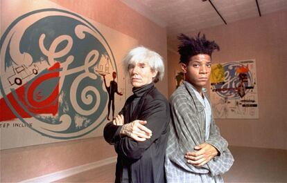 Los artistas Andy Warhol (izquierda), y Jean-Michel Basquiat, posan delante de varias obras que fueron vendidas en su día por elevados precios, en septiembre de 1985.