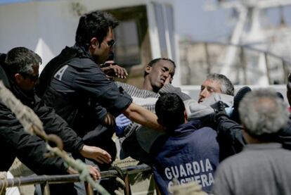Policías y guardacostas italianos transportan a un refugiado herido tras su llegada a la isla de Lampedusa.