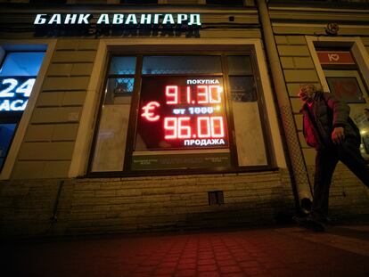 Un hombre camina junto a un panel con información sobre la divisa rusa