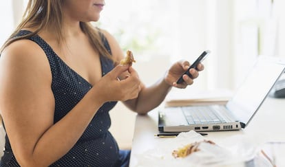 Una mujer desayuna mientras mira el móvil. 