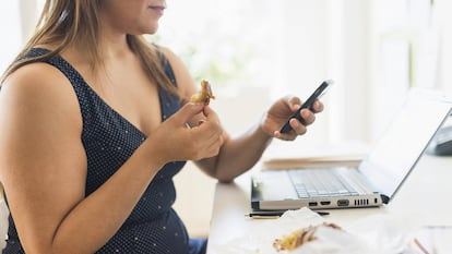 Una mujer desayuna mientras mira el móvil.