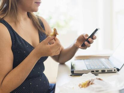 Una mujer desayuna mientras mira el móvil. 