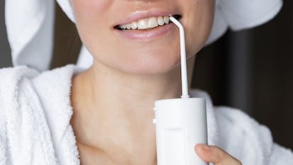 Mujer joven con un irrigador dental recién salida de la ducha con el albornoz y una toalla en la cabeza.