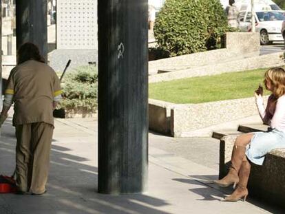 Una limpiadora recoge colillas mientras otra mujer fuma en la vía pública en Madrid.