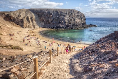 El sureste de Lanzarote se ve dorado en su arena, se siente frío por un Atlántico de tonos azules verdosos, sabe a salitre, suena a viento alisio y huele a arena quemada por el sol africano. Con Fuerteventura y el islote de Lobos al fondo, la caleta de Papagayo, la más fotogénica y aplacerada, la que da nombre al resto de playas del monumento natural de los Ajaches, sirvió hasta mediados del siglo pasado como fondeadero. Los niños gustan de su media luna bien trazada; otros practican snorkel en sus laterales. Pero todo se revela secundario frente a la panorámica que se divisa desde la terraza natural que otorga el acantilado, junto a El Chiringuito. El placer visual encuentra durante el crepúsculo su máxima expresión. <p><b>Acceso:</b> desde el enclave de Playa Blanca sale un ramal primero de asfalto y luego de tierra. Peaje medioambiental (3 euros), solo a coches, de 9.00 a 16.00 (hasta las 17.30 a partir de junio). Alquilan bicicletas en Papagayo Bike (papagayobike.com). La bajada ha sido acondicionada con escalones y postes de madera ensogados.</p>