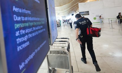 Un agente de seguridad de Trablisa pasa ante uno de los paneles informativos de la T4 de Madrid-Barajas que advierte de la huelga en los controles del equipaje.
