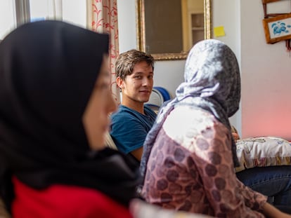 El joven afgano Hujjat, junto a dos de sus hermanas, en el piso de acogida donde vive con toda su familia en España.