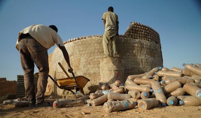 Dos hombres trabajan en la construcción de una vivienda hecha con botellas de plástico en el campamento de Tinduf.