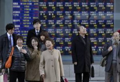 Viandantes caminan frente a una pantalla que muestra los indicadores de las principales bolsas mundiales, en Tokio, Japón. EFE/Archivo