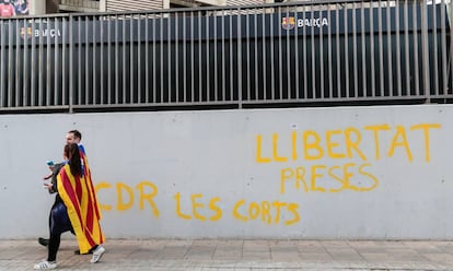 Dos manifestantes independentistas caminan este miércoles por delante del Camp Nou, en Barcelona,ante una pintada que reza "libertad presos cdr Les Corts".