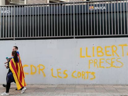 Dos manifestantes independentistas caminan este miércoles por delante del Camp Nou, en Barcelona,ante una pintada que reza "libertad presos cdr Les Corts".