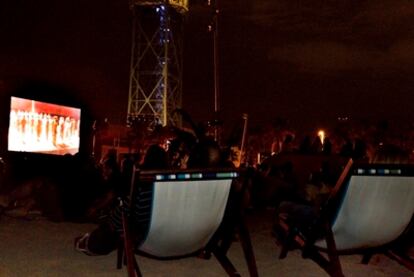 Dos espectadores de la ópera 'Carmen', en sus tumbonas en la playa de la Barceloneta, en Barcelona.