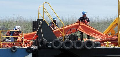 Varios trabajadores llevan las barreras de contención a una nave más pequeña en el Paso Sur del Mississippi en Port Eads, en Lousiana, en una imagen tomada el jueves, 29 de abril.