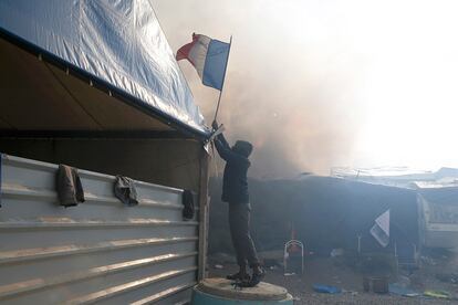 Un migrante coge una bandera francesa antes de ser devorada por las llamas durante el incendio en el campamento de Calais.