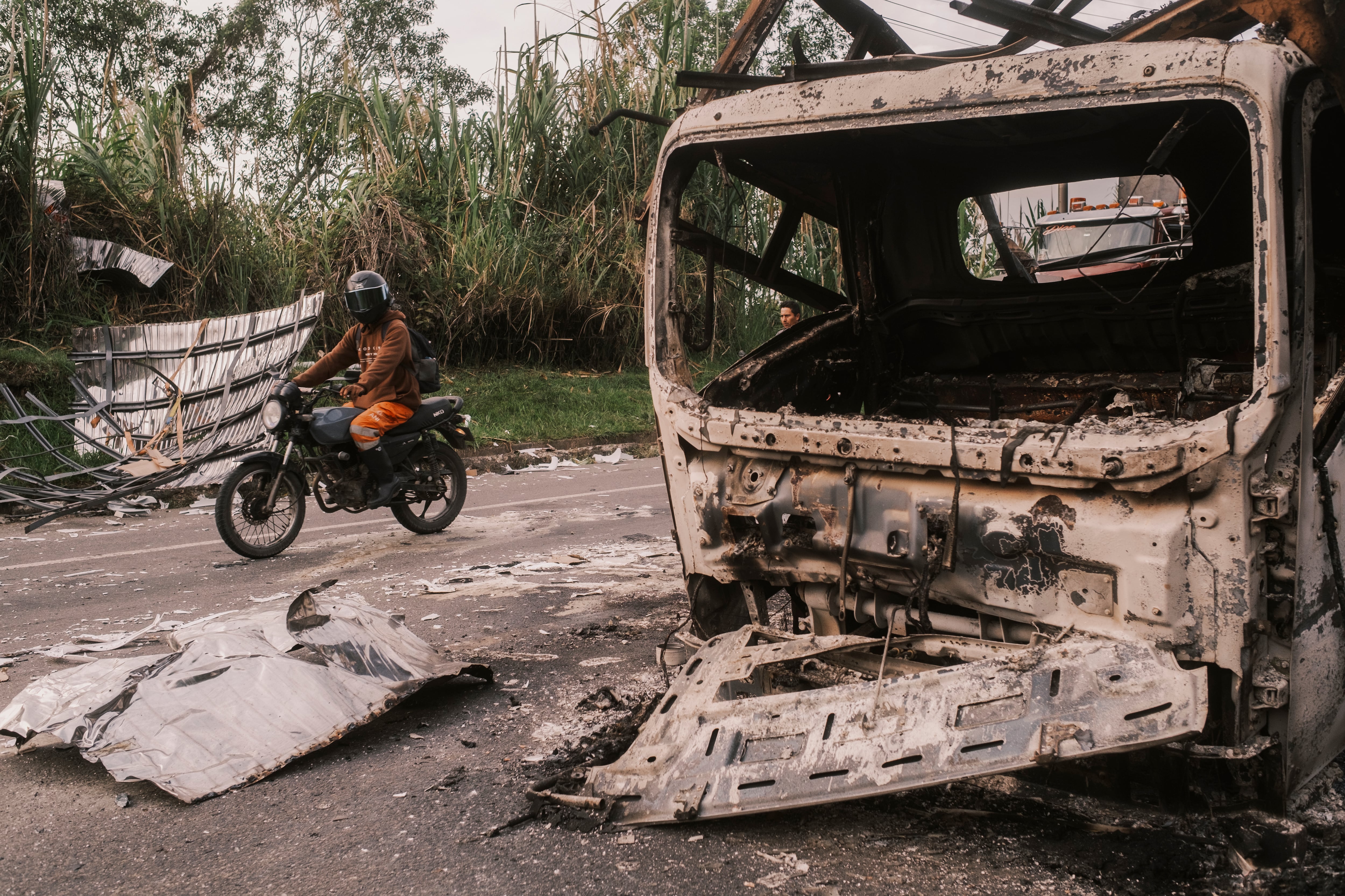 Un motociclista junto a los restos de un vehículo  detonado con explosivos en la vía Panamericana, en La Agustina, Cauca, el 29 de abril.