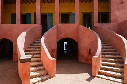 Isla de Gorea (Senegal).
Con 28 kilómetros cuadrados, este es un lugar extraño, a la vez que conmovedor e inquietante. Símbolo del comercio de esclavos en el Atlántico entre los siglos XV y XIX, desde aquí partieron millones de africanos esclavizados, encadenados a los barcos negreros, para no regresar nunca. La isla está apenas a 20 minutos en ferri de la costa de Dakar, la moderna y turbulenta capital de Senegal. Hoy es un lugar pacífico que invita a reflexionar sobre uno de los periodos más oscuro de la historia de la humanidad, por lo que la visita a ciertos lugares históricos de la isla es imprescindible.
No hay carreteras asfaltadas, ni automóviles, solo callejones estrechos con buganvillas y edificios de ladrillo de época colonial con balcones de hierro forjado. El pasado de Gorea se cuenta en la Casa de los Esclavos (en la imagen), uno de los pocos edificios del siglo XVIII que sobreviven aquí. Construido en 1786, renovado en 1990, su característica más famosa es la escalofriante “puerta a ninguna parte”, que se abre directamente desde el almacén del piso inferior hacia el mar y es donde en su día atracaban los barcos que se llevaban a los esclavos. No es el único sitio histórico de este tipo a lo largo de la costa de África occidental, pero aquí hay algo intangible que evoca el horror y la crueldad de esa parte de la historia.
A pesar de todo, Gorea, patrimonio mundial de la Unesco desde 1978, es ahora el foco de una activa comunidad de artistas, con estudios repartidos por todo su territorio, de una naturaleza salvaje.