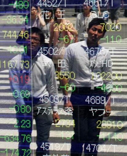 Dos japoneses pasan delante de un panel con información sobre los índices de Tokio, que se han situado en su peor nivel desde marzo