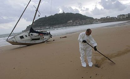 Un operario limpiaba ayer de chapapote la playa de La Concha, junto a un velero que dejó varado el temporal.