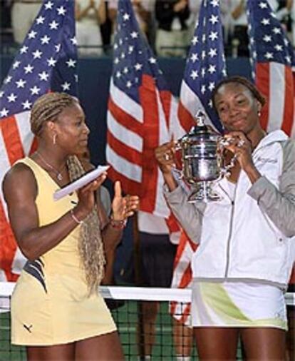 La tenista Venus Williams (a la derecha) sujeta el trofeo como ganadora del Open de EE UU junto a su derrotada hermana Serena que aplaude a su lado.