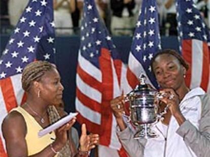 La tenista Venus Williams (a la derecha) sujeta el trofeo como ganadora del Open de EE UU junto a su derrotada hermana Serena que aplaude a su lado.