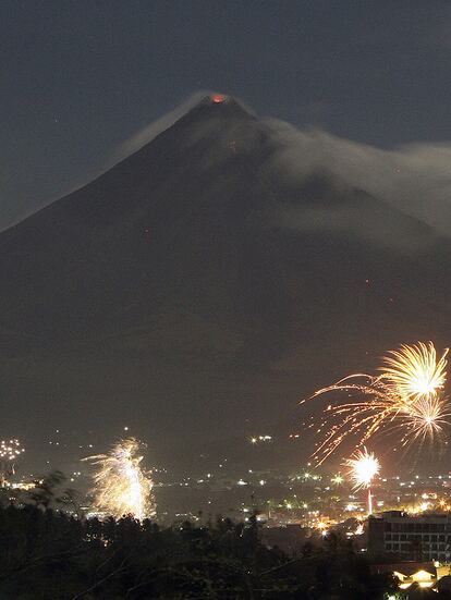 Las luces de los fuegos artificiales contrastan con los fuegos del volcán Mayón en la ciudad de Legazpi en Filipinas