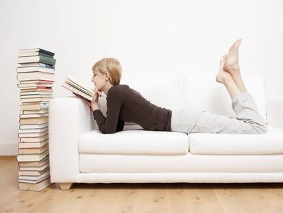 Una mujer lee un libro en un sofá.
