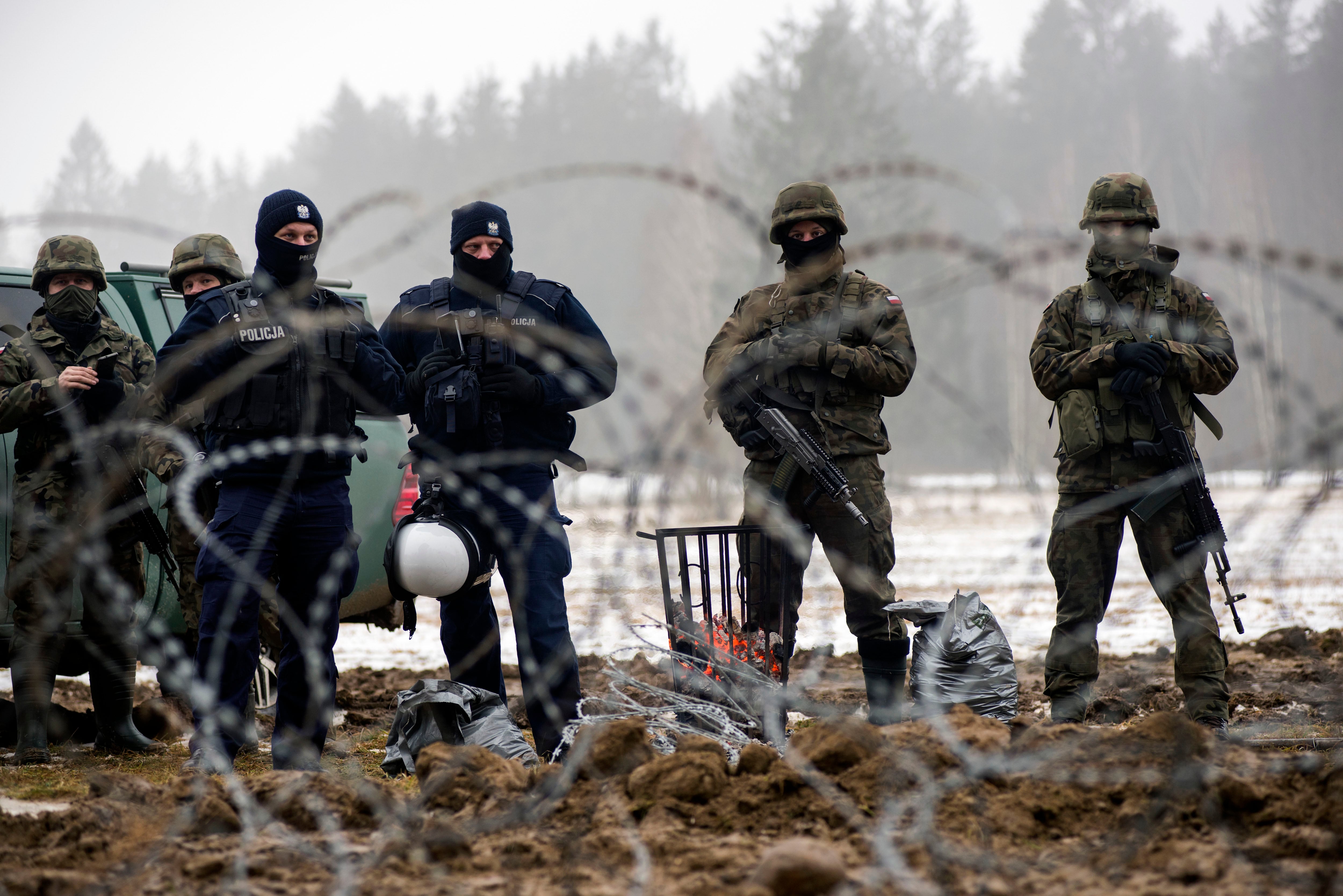 Varios guardias fronterizos armados y agentes de policía vigilan la línea fronteriza de Polonia con Bielorrusia en enero de 2022.  