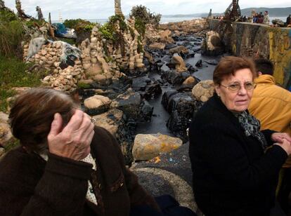 Los vecinos de Camelle (A Coruña) aparecen desolados por las consecuencias en el puerto de la localidad. Al fondo se ven varias esculturas realizadas con piedras por el alemán Manfred Gnadinger 'Man'. Man se pasó 40 años viviendo como un anacoreta en las costas de Camelle, murió en diciembre de 2002, sólo un mes después del naufragio del Prestige y de la llegada de las primeras mareas negras.