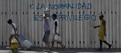 Varios venezolanos acarrean agua ante una pintada en una calle de Caracas que pregunta: “¿La normalidad es un privilegio?”.
