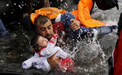 Un refugiado sirio coge a un ni&ntilde;o en su llegada a la isla griega de Lesbos.