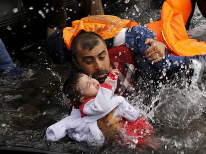 Un refugiado sirio coge a un ni&ntilde;o en su llegada a la isla griega de Lesbos.