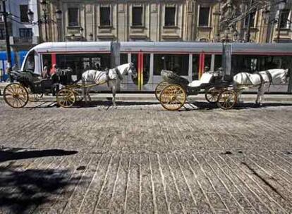 El tranvía pasa junto a los tradicionales coches de caballos por la avenida de la Constitución.