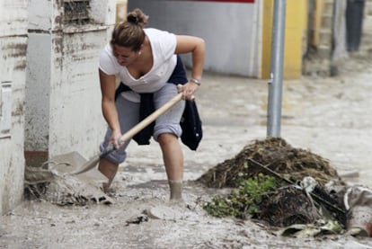 Una mujer de Aguilar de la Frontera trata de limpiar a paletadas la puerta de su casa después de las fuertes lluvias.