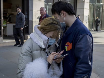 Una pareja asiática hace uso de su teléfono móvil en una calle de Londres durante la crisis del coronavirus.