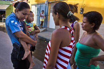 Lidia, policía militar, pregunta a unas vecinas si conocen al niño que lleva en brazos. Un vecino lo llevó a la UPP (Unidad de Policía Pacificadora) de Nova Brasilia en el Complexo de Alemao tras encontrarlo perdido.