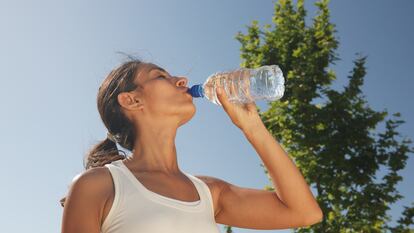 Una mujer bebe de una botella de agua de plástico.