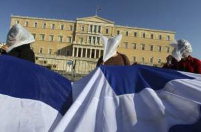 Unas personas sostienen una bandera de Grecia y llevan bolsas de plástico sobre sus cabezas para representar la "asfixia" durante una manifestación. EFE/Archivo