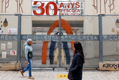 Dos personas pasan ante las puertas cerradas de un colegio cuyas clases se suspendieron este jueves ante la alerta meteorológica naranja en la ciudad de Valencia.