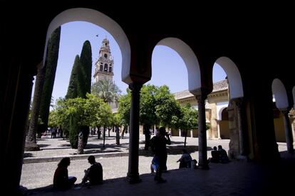 Un grupo de turistas sentados en el Patio de los Naranjos, al fondo la torre de la mezquita.