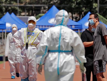 Un policía en traje protector vigila a vecinos del mercado de Xinfadi que acuden a hacerse una prueba de coronavirus en un estadio de Pekín.
