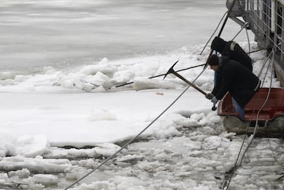 Dos hombres rompen bloques de hielo junto a un edificio flotante.