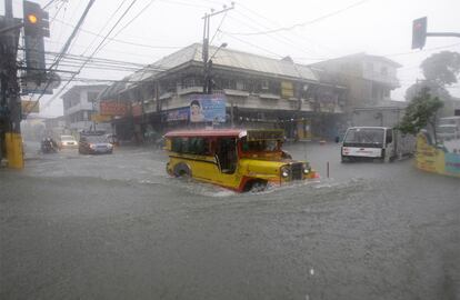 Un jeep con pasajeros intenta cruzar una intersección inundada tras el paso del tifón Muifa en Manila.