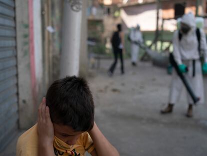 Un niño se tapa los oídos mientras un voluntario desinfecta una calle en Río de Janeiro.