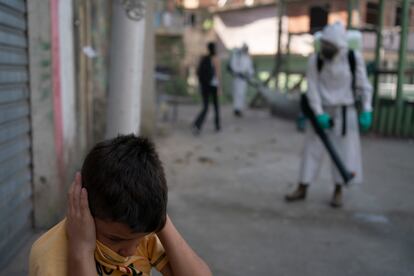 Un niño se tapa los oídos mientras un voluntario desinfecta una calle en Río de Janeiro.