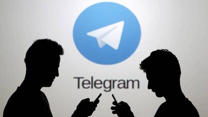 Dos hombres consultan sus teléfonos móviles delante del logotipo de la aplicación Telegram.
 